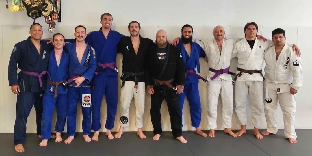 Gi jiu jitsu students drilling a standing pass beneath the CPJJ wall logo in Norfolk